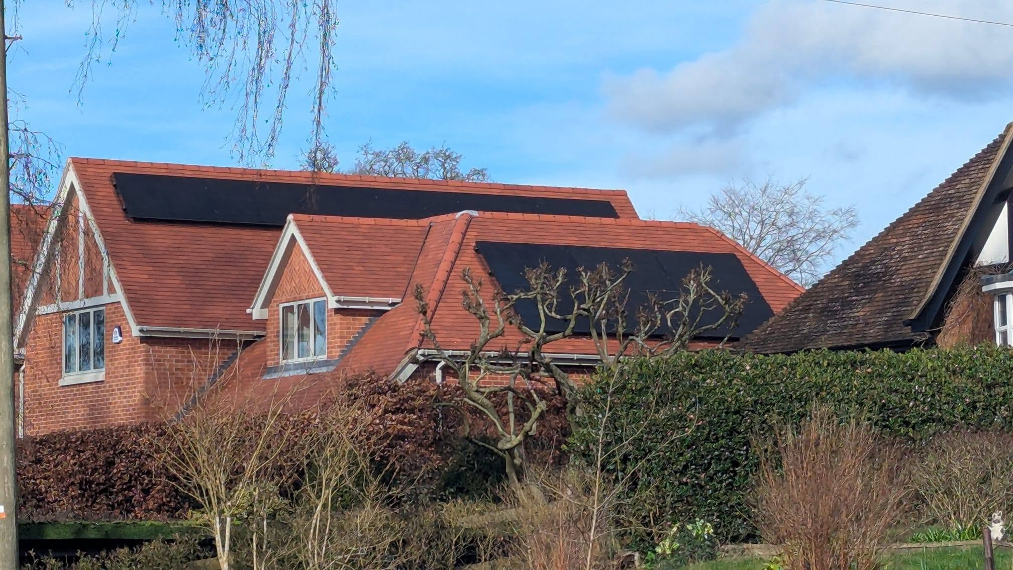 Solar panels fitted to the tiled roof of a red-brick residential home.